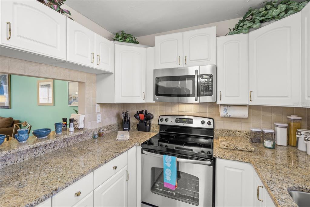 A kitchen features white cabinets, granite countertops, stainless steel appliances, and a pass-through window — 1630 STICKNEY POINT ROAD UNIT 101, SARASOTA, FL
