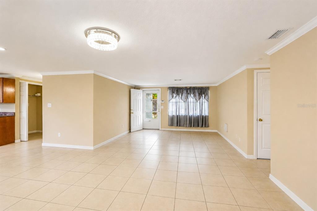 An open-concept living area features beige walls, light tile flooring, and a white front door — 4128 BADEN DRIVE, HOLIDAY, FL