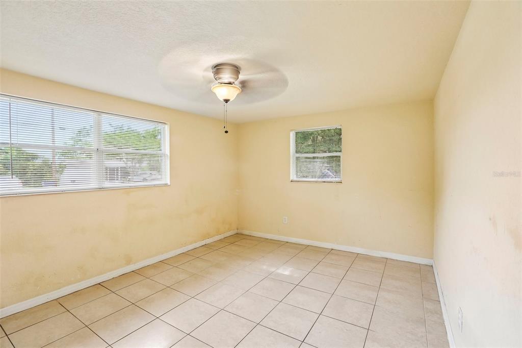An empty room with beige walls, tiled floors, a ceiling fan, and two windows — 4128 BADEN DRIVE, HOLIDAY, FL