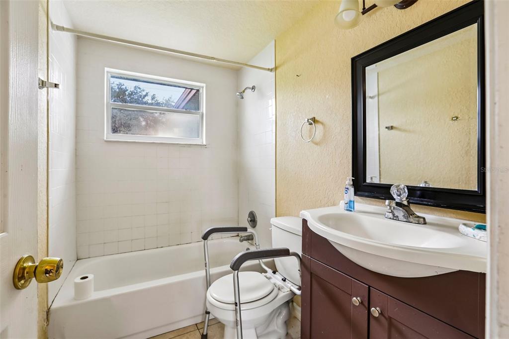 A bathroom features a white tub-shower combo, a toilet with safety rails, and a vanity — 4128 BADEN DRIVE, HOLIDAY, FL