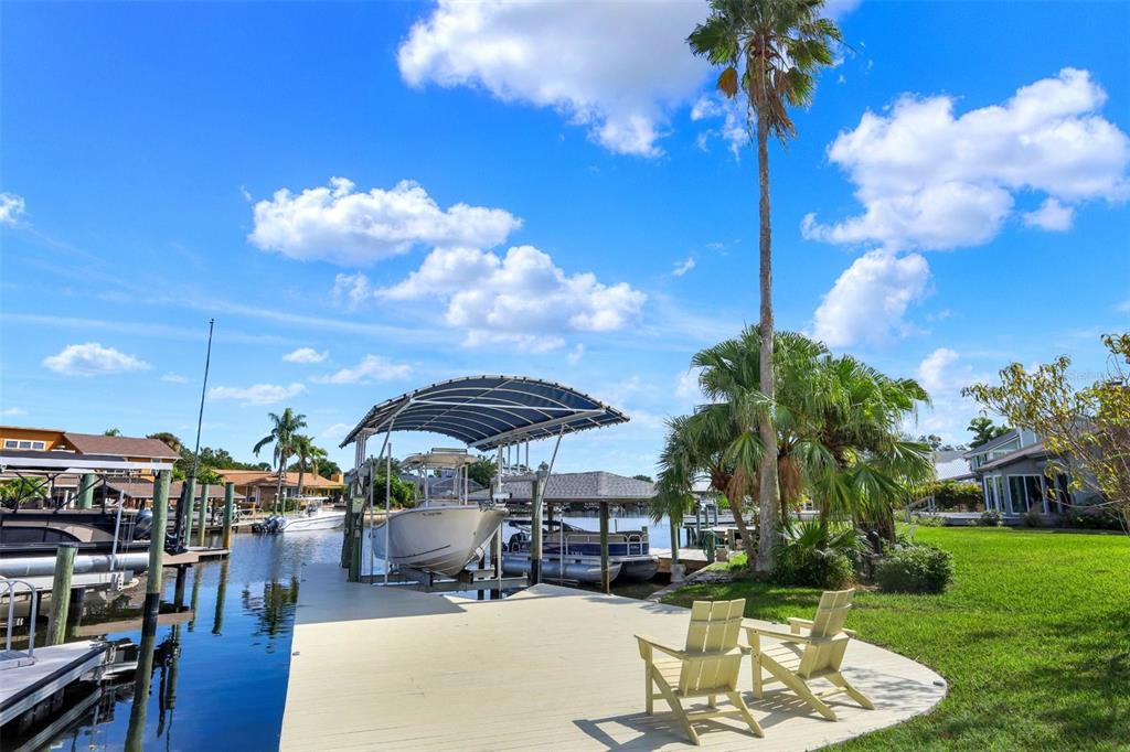 A boat dock with a covered lift and two chairs sits along a canal — 301 QUAY ASSISI, NEW SMYRNA BEACH, FL