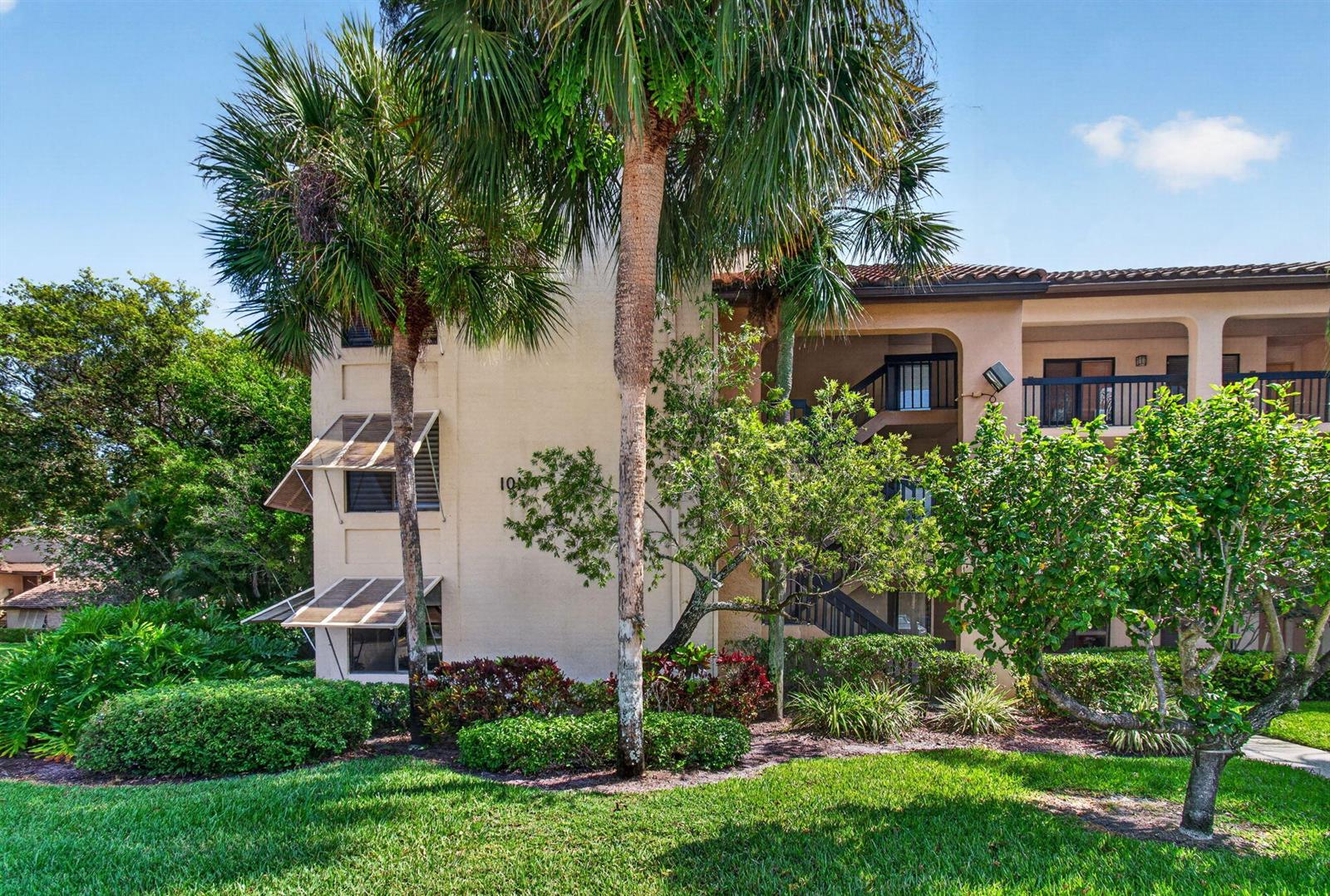 A multi-story apartment building features beige stucco walls, dark railings, and lush landscaping — 10174 Mangrove Drive # 201, Boynton Beach FL 33437, BOYNTON BEACH, FL