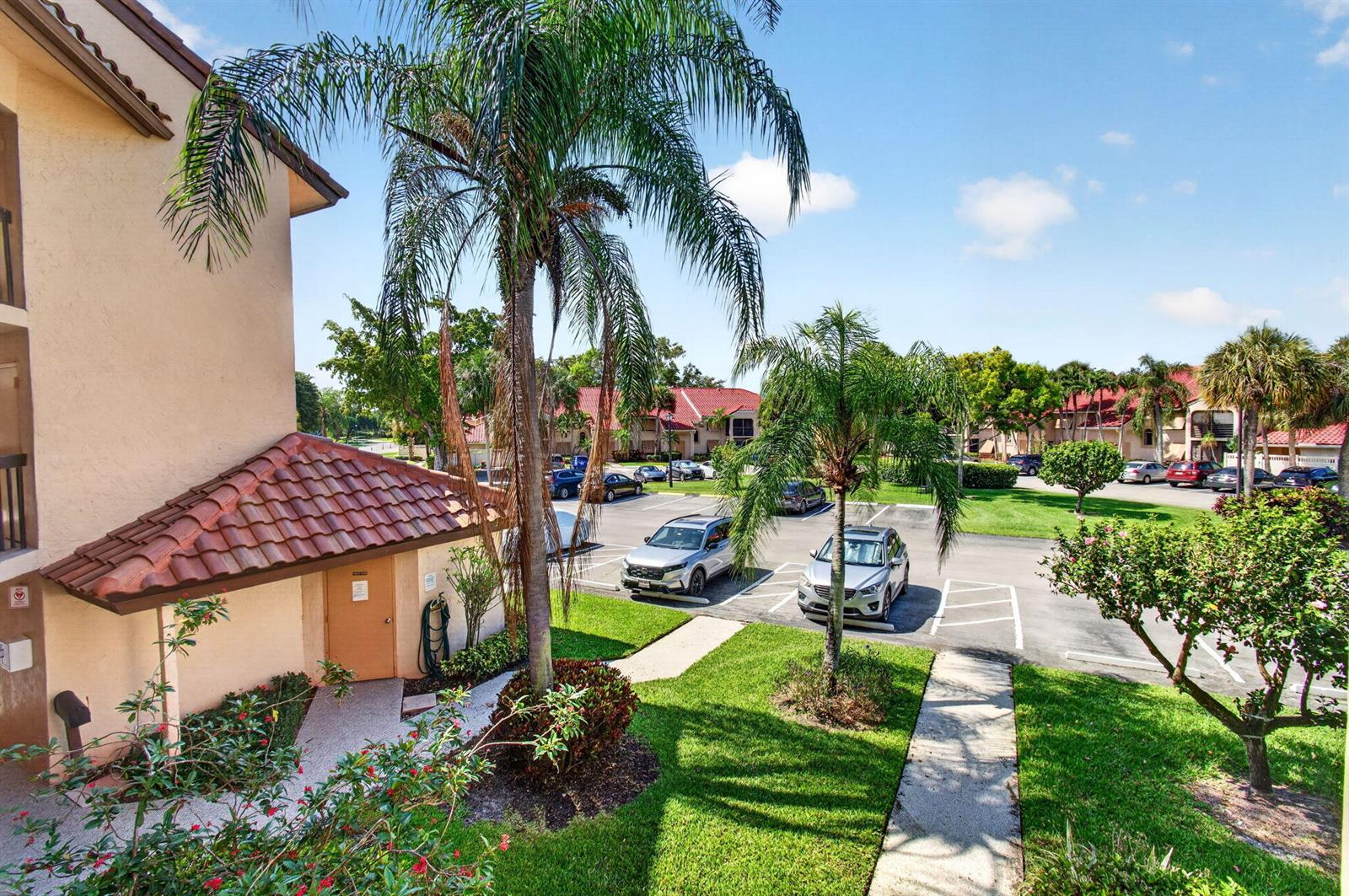 An outdoor view of a residential complex with a parking lot, palm trees, and landscaping — 10174 Mangrove Drive # 201, Boynton Beach FL 33437, BOYNTON BEACH, FL
