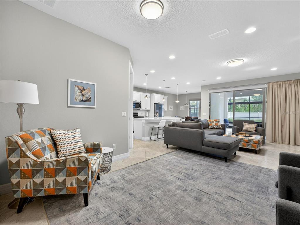 A living room with a patterned armchair, gray sectional sofa, and an open-concept kitchen — 11708 MEADOW GROVE CIRCLE, ORLANDO, FL