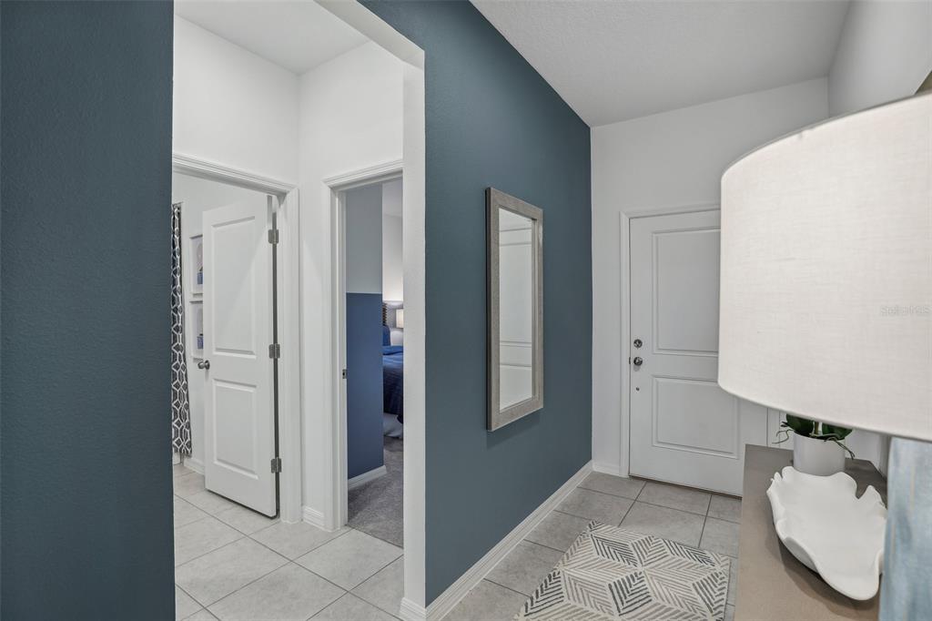 A hallway with blue accent walls, tile flooring, a mirror, and doors leading to other rooms — 23599 GRINDSTONE WAY, SORRENTO, FL