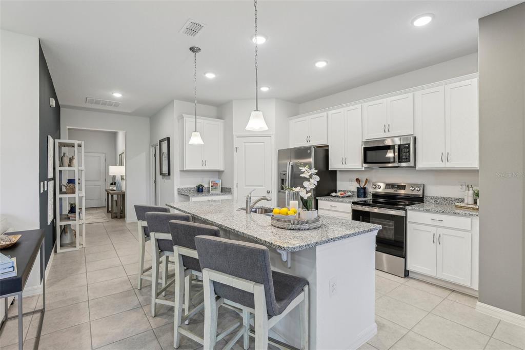 A kitchen features white cabinets, granite countertops, a central island with bar seating, and tile flooring — 23599 GRINDSTONE WAY, SORRENTO, FL