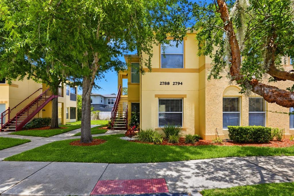 A yellow two-story apartment building features exterior staircases and a landscaped front lawn — 2788 CLUB CORTILE CIRCLE UNIT A, KISSIMMEE, FL