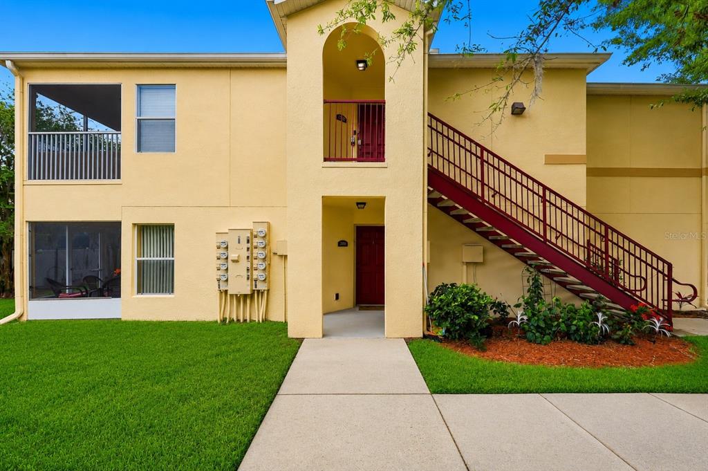 A two-story yellow apartment building features a screened-in patio, an exterior staircase, and utility meters — 2788 CLUB CORTILE CIRCLE UNIT A, KISSIMMEE, FL