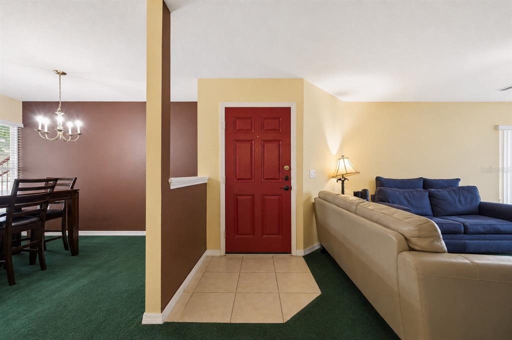 A red front door opens into a living area with green carpet and a dining space — 2788 CLUB CORTILE CIRCLE UNIT A, KISSIMMEE, FL
