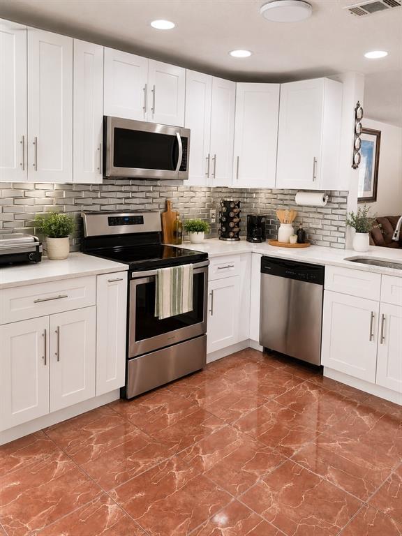 A kitchen with white cabinets, stainless steel appliances, gray subway tile backsplash, and reddish-brown flooring — 499 CHICAGO WOODS CIRCLE, ORLANDO, FL