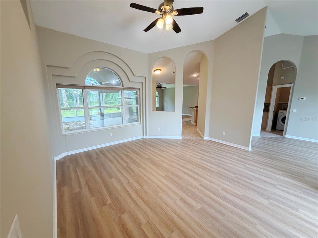 An empty living room features light wood-look flooring, arched wall niches, and a large window — 10 ELLIOT PLACE, PALM COAST, FL
