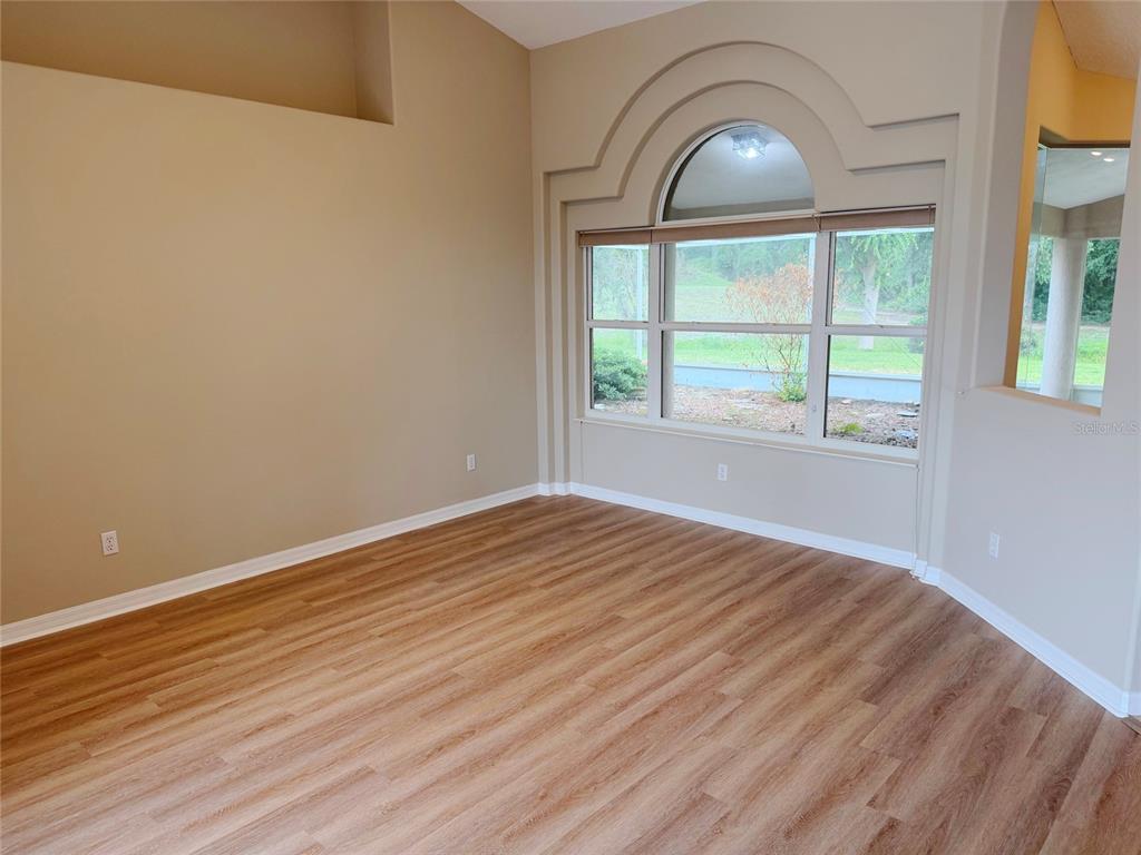 An empty room features light wood-look flooring, beige walls, and a large arched window — 10 ELLIOT PLACE, PALM COAST, FL