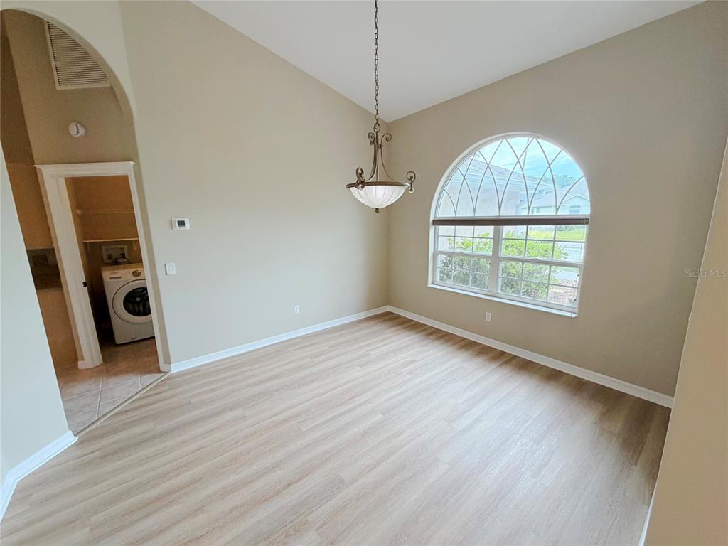 An empty dining room features light wood-look flooring, a vaulted ceiling, and an arched window — 10 ELLIOT PLACE, PALM COAST, FL