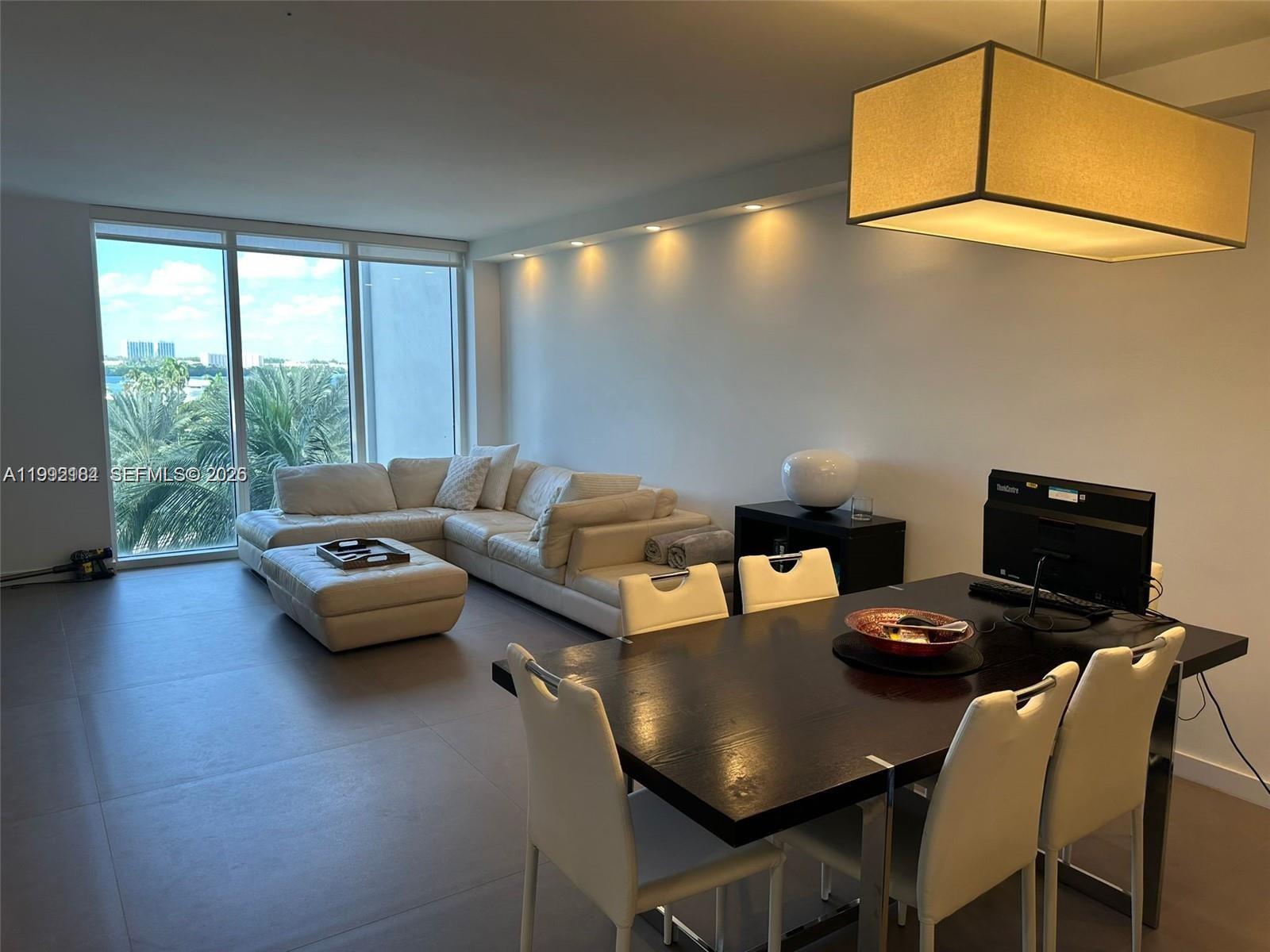A modern living and dining area features a white sectional sofa, dark table, and floor-to-ceiling windows — 10275 Collins Ave # 523, Bal Harbour FL 33154, BAL HARBOUR, FL