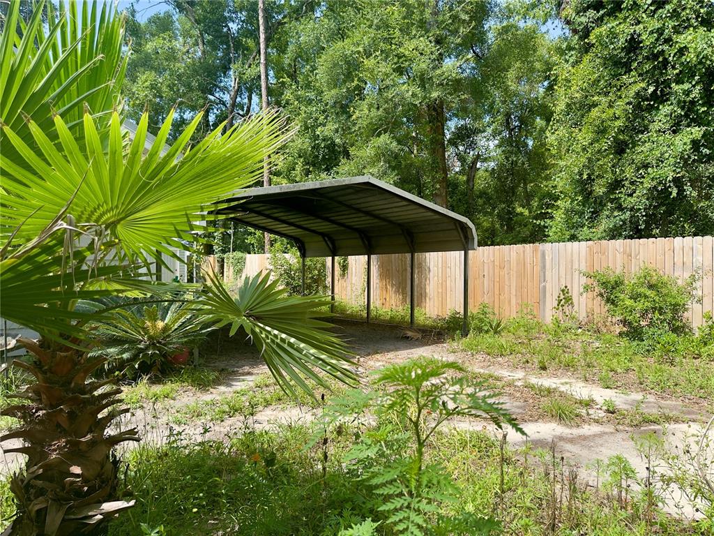 A metal carport stands in a grassy backyard next to a wooden fence and palm tree — 930 NE 14TH AVENUE, TRENTON, FL