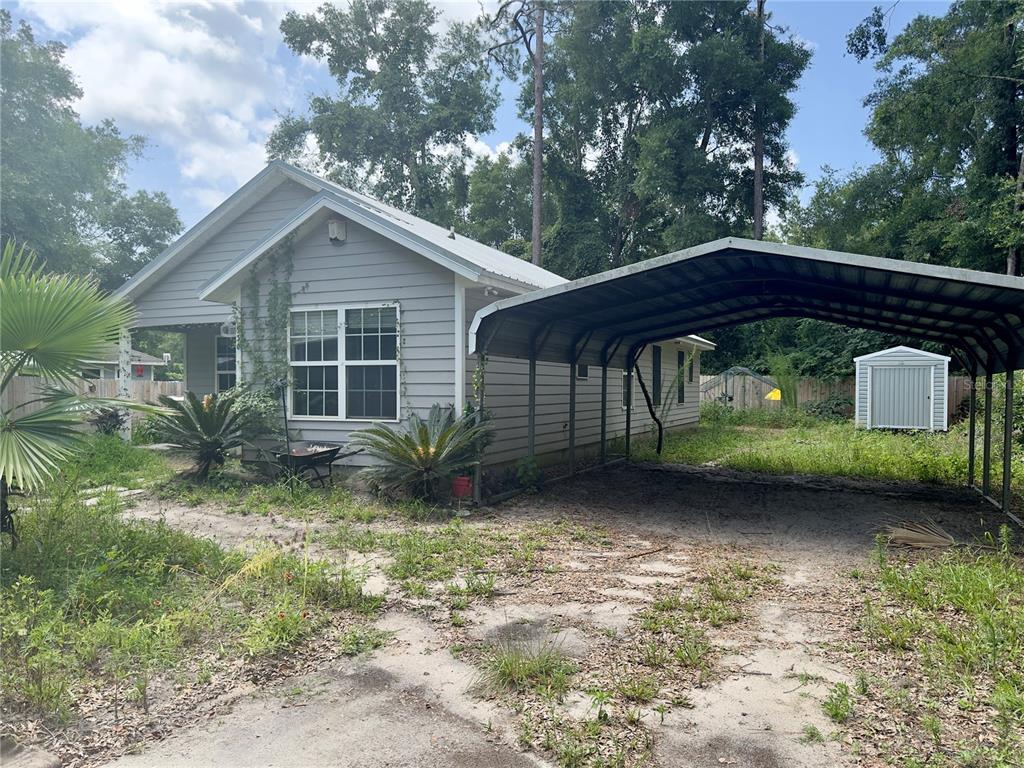 A gray house with a metal roof and a large carport stands on a sandy lot — 930 NE 14TH AVENUE, TRENTON, FL