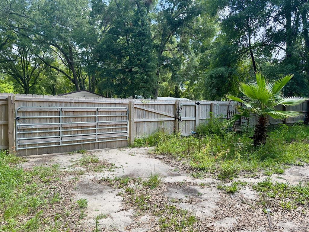 A wooden fence with a metal gate encloses a sandy yard with a small palm tree — 930 NE 14TH AVENUE, TRENTON, FL