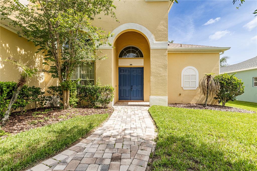 A paved walkway leads to the blue double front doors of a yellow stucco house — 2718 KNIGHTSBRIDGE ROAD, CLERMONT, FL