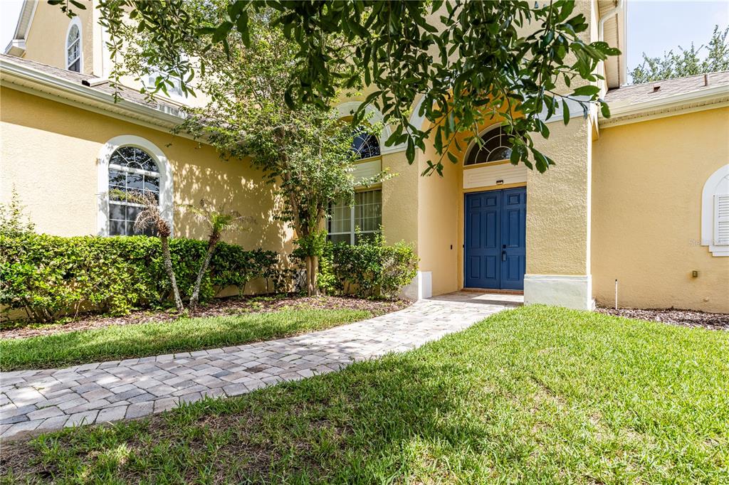 A yellow stucco house features a blue double front door and a stone walkway — 2718 KNIGHTSBRIDGE ROAD, CLERMONT, FL