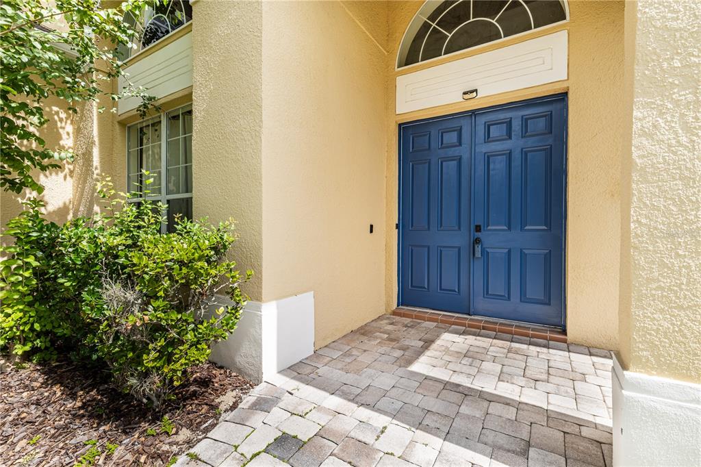 A blue double front door is set in a tan stucco wall with a brick walkway — 2718 KNIGHTSBRIDGE ROAD, CLERMONT, FL