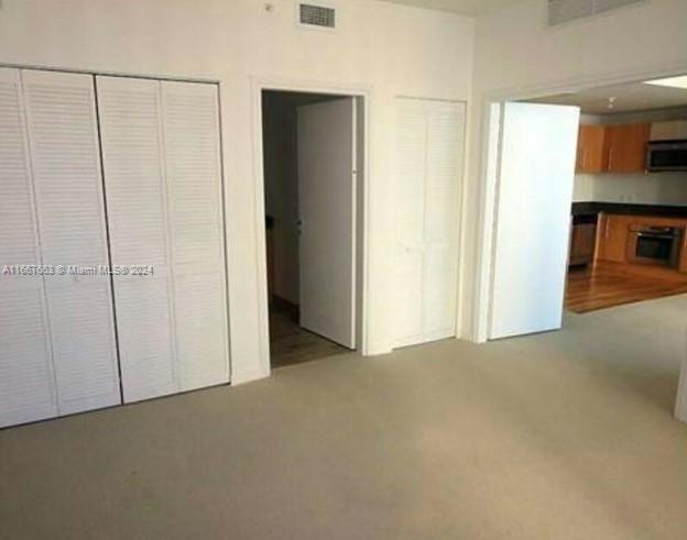 An interior view shows a carpeted room with louvered closet doors and an adjacent kitchen — 300 S Biscayne Blvd # 1703, Miami FL 33131, MIAMI, FL