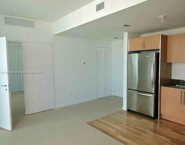 A kitchen area with light wood cabinets and a stainless steel refrigerator next to a hallway — 300 S Biscayne Blvd # 1703, Miami FL 33131, MIAMI, FL