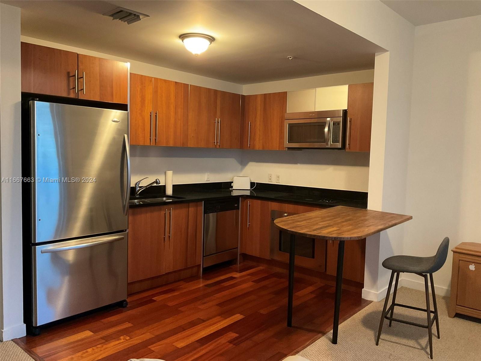 A kitchen features wood cabinets, stainless steel appliances, black countertops, and a small wooden table — 300 S Biscayne Blvd # 1703, Miami FL 33131, MIAMI, FL