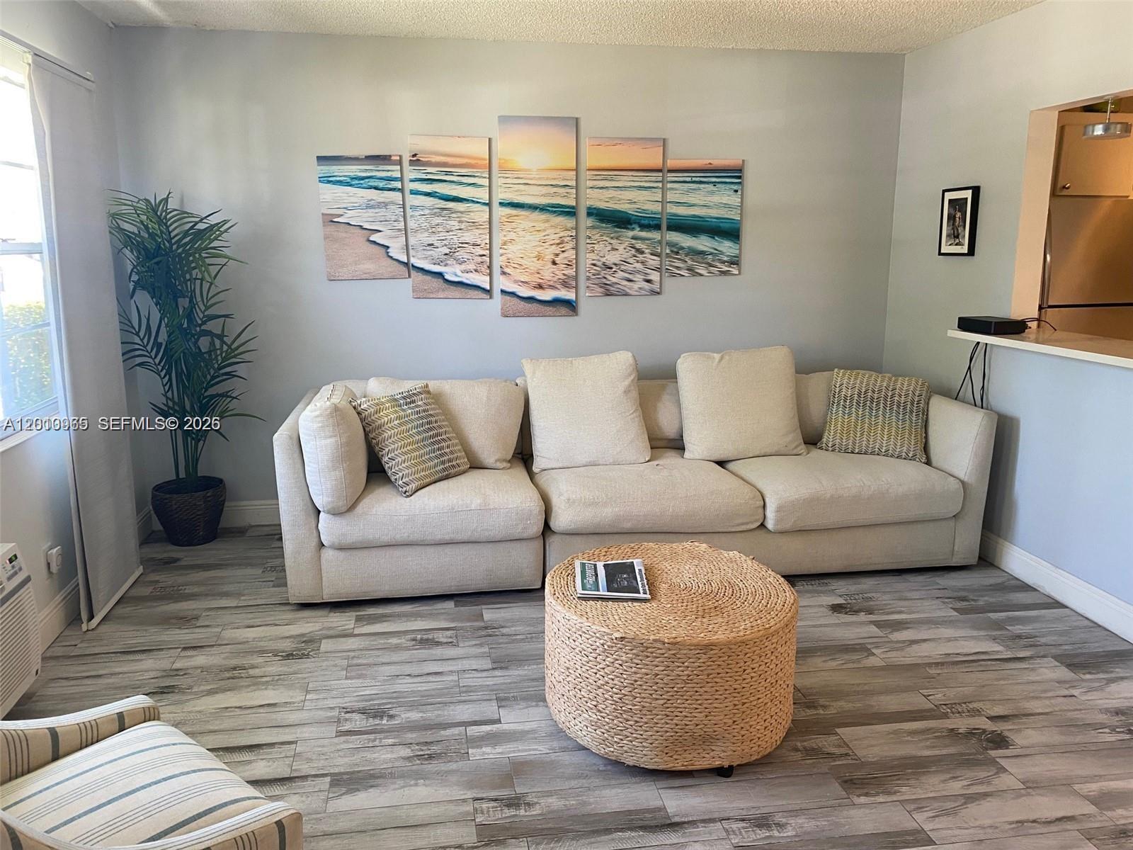 A living room features a beige sectional sofa, a round woven ottoman, and beach-themed wall art — 172 Prescott I # 172, Deerfield Beach FL 33442, DEERFIELD BEACH, FL