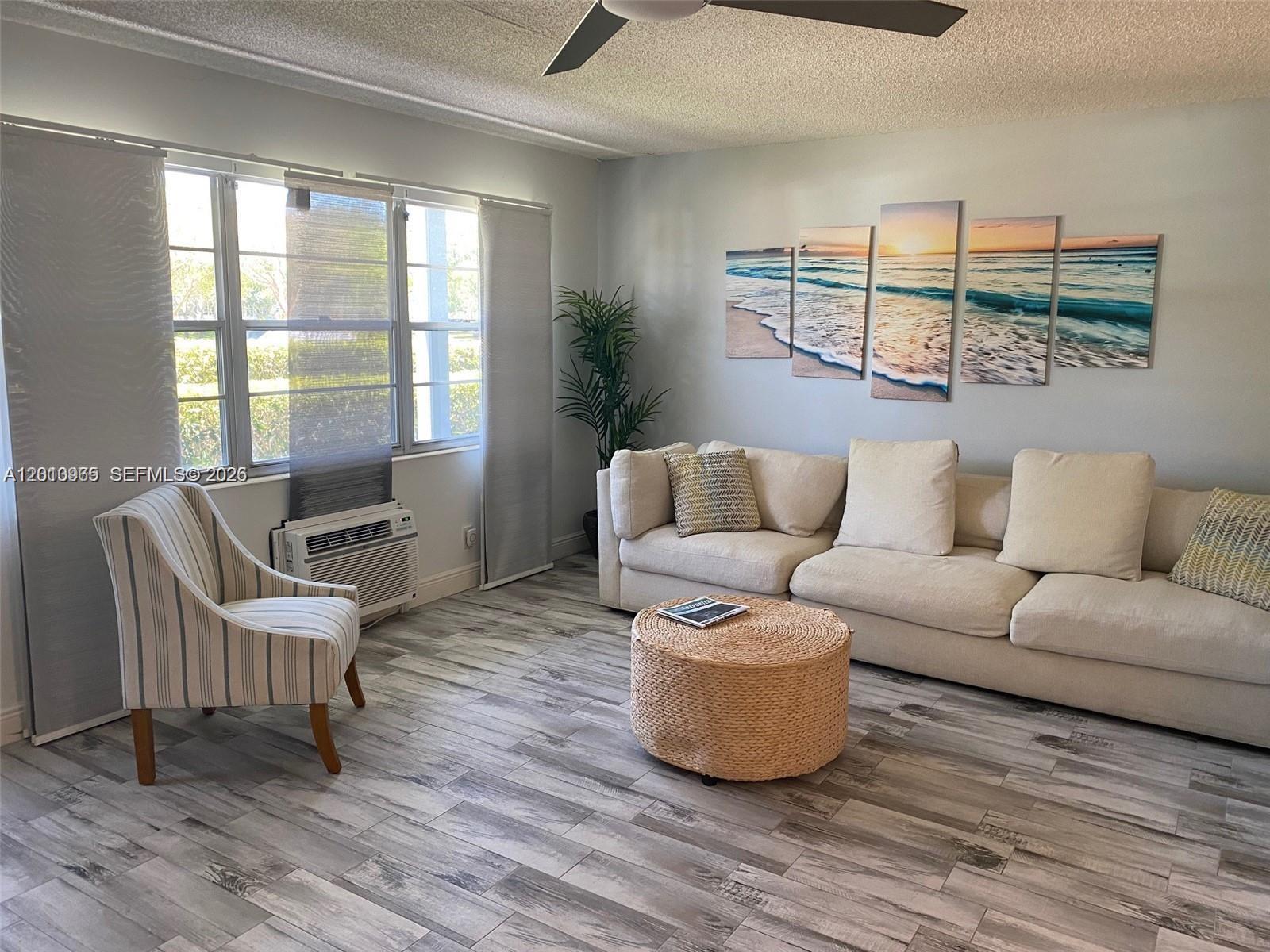A living room features a beige sectional sofa, a round woven ottoman, and wood-look flooring — 172 Prescott I # 172, Deerfield Beach FL 33442, DEERFIELD BEACH, FL