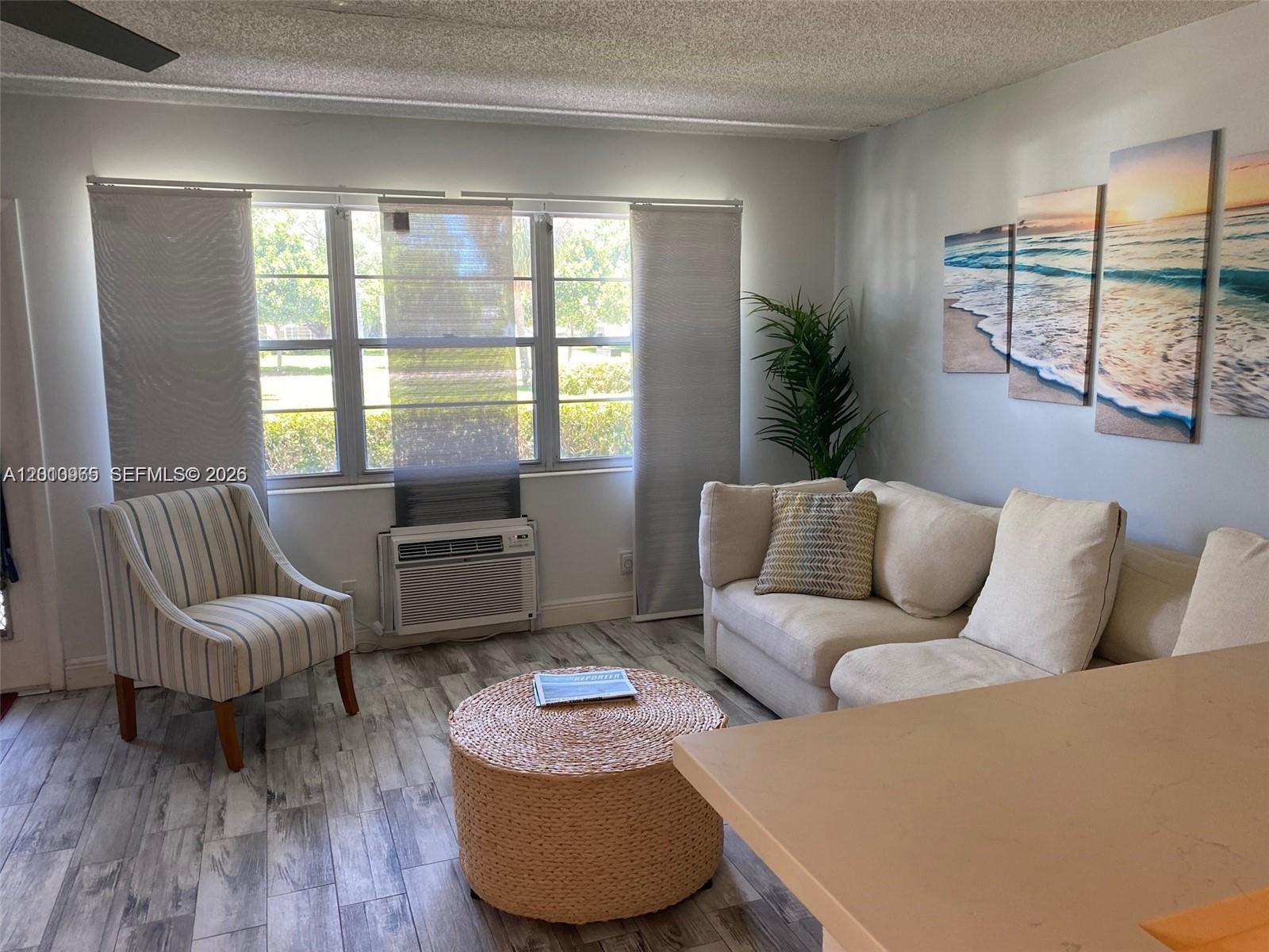 A living room features a beige sofa, striped armchair, woven ottoman, and wall-mounted beach artwork — 172 Prescott I # 172, Deerfield Beach FL 33442, DEERFIELD BEACH, FL