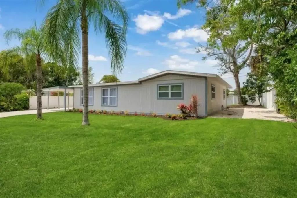 A single-story house with light-colored siding sits on a grassy lot with palm trees — 2539 TRINIDAD STREET, SARASOTA, FL
