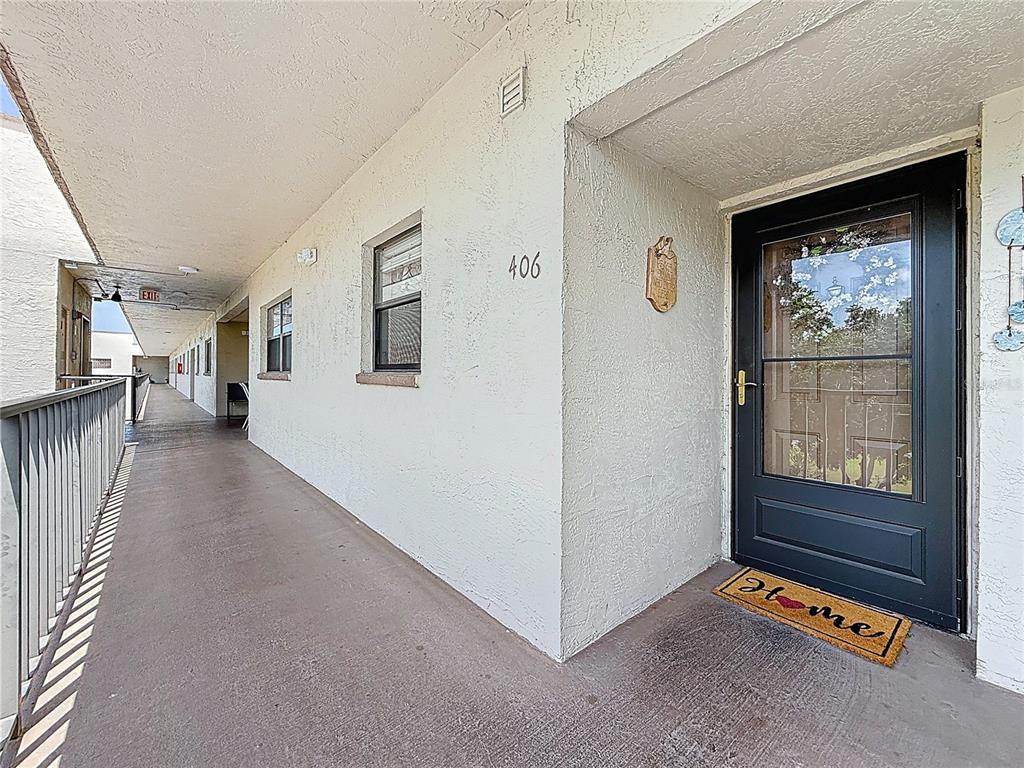 An exterior view of an apartment building hallway with a black front door and balcony — 5920 80TH STREET N UNIT 406, ST PETERSBURG, FL