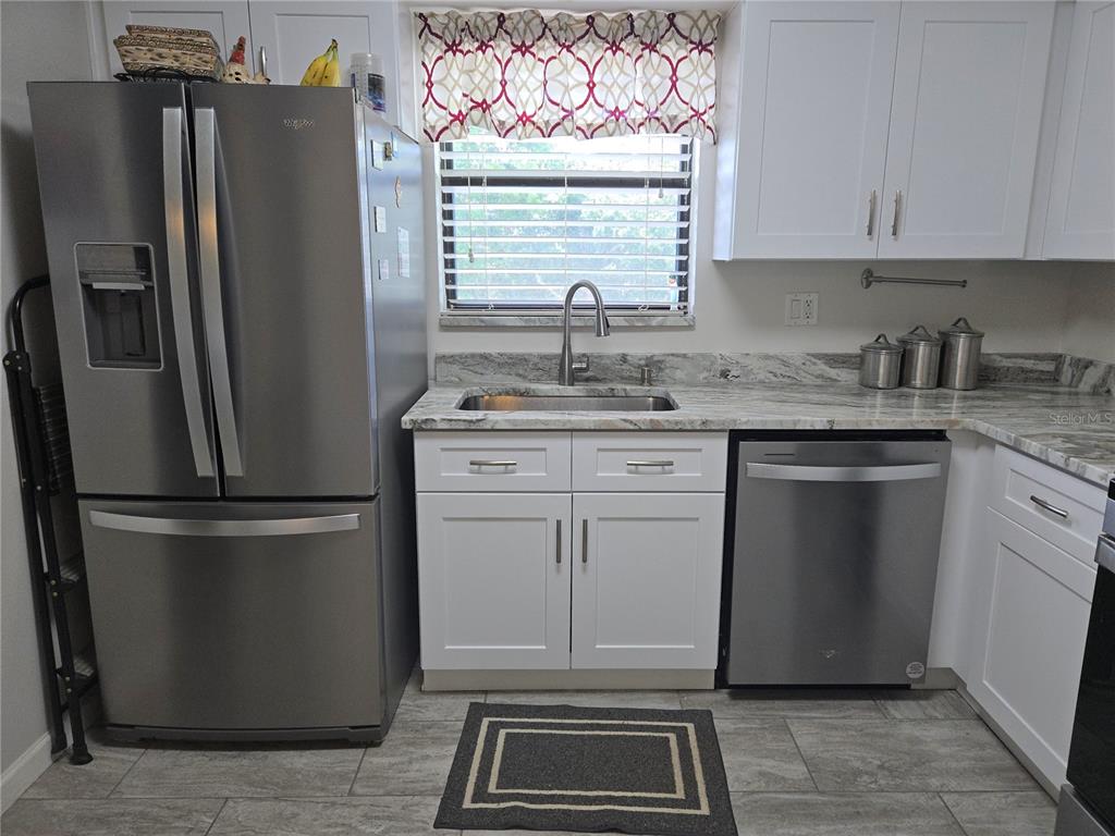 A kitchen features white cabinets, stainless steel appliances, a sink, and patterned stone countertops — 5920 80TH STREET N UNIT 406, ST PETERSBURG, FL