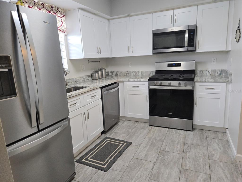A kitchen features white cabinets, stainless steel appliances, and light-colored stone countertops — 5920 80TH STREET N UNIT 406, ST PETERSBURG, FL