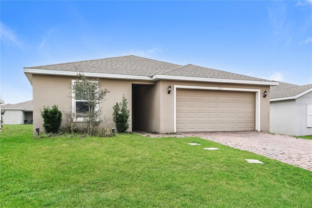 A single-story tan house with a two-car garage and a paved driveway — 1473 LUCERNE LOOP ROAD NE, WINTER HAVEN, FL