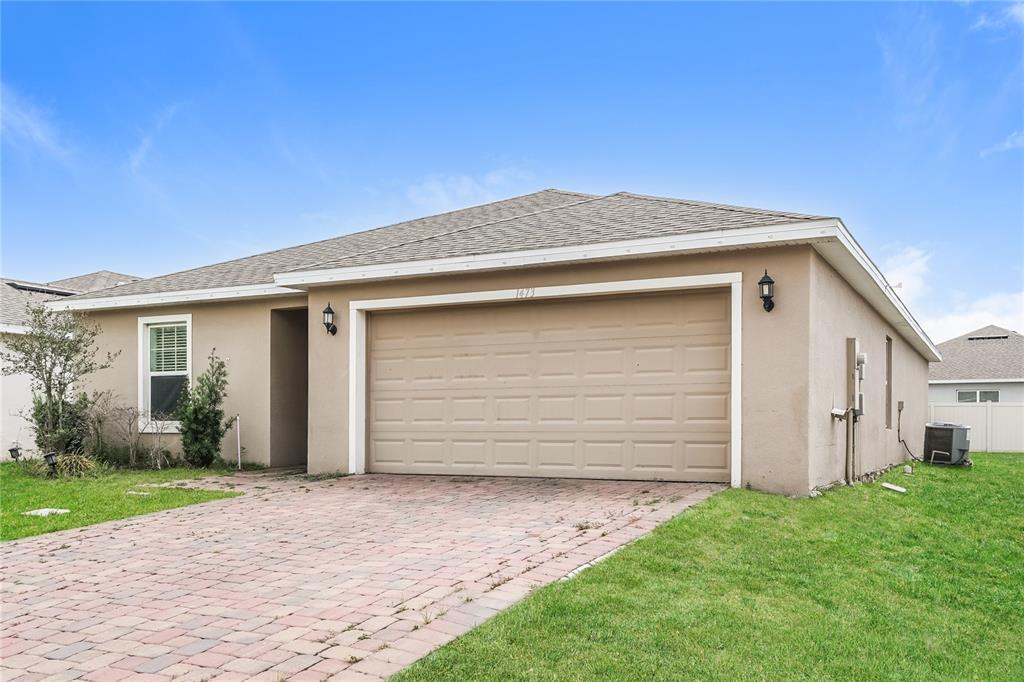 A single-story house with a beige stucco exterior, a two-car garage, and a paver driveway — 1473 LUCERNE LOOP ROAD NE, WINTER HAVEN, FL