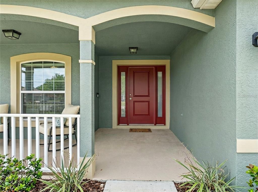 A covered front porch with a red door, white railing, and light green stucco walls — 9696 SE 157TH PLACE, SUMMERFIELD, FL
