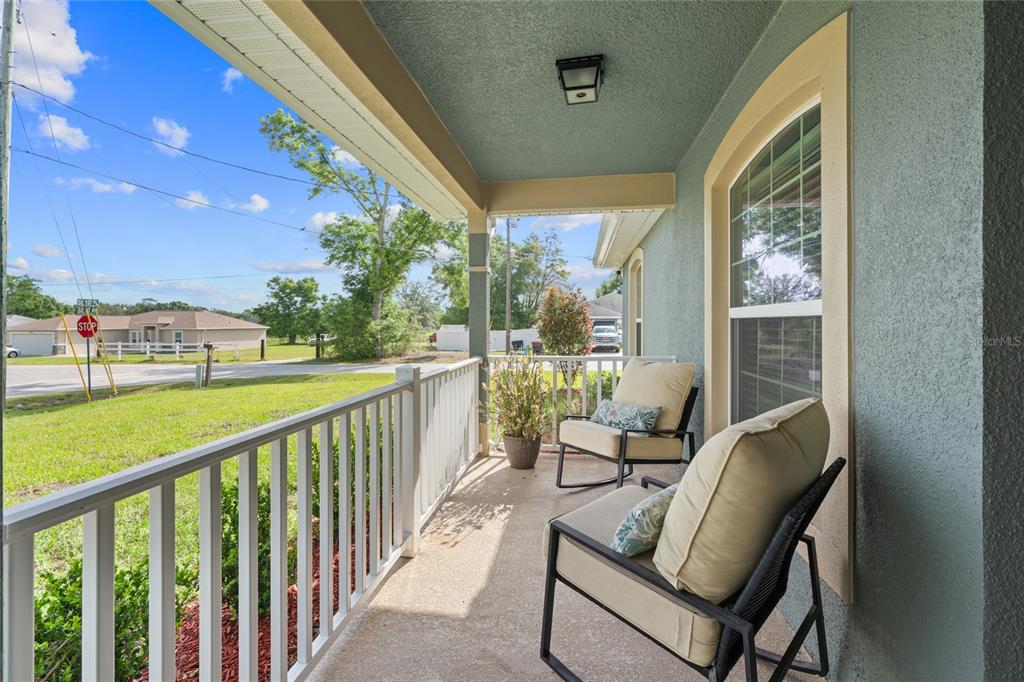 A covered front porch features a white railing, two cushioned chairs, and a view outdoors — 9696 SE 157TH PLACE, SUMMERFIELD, FL