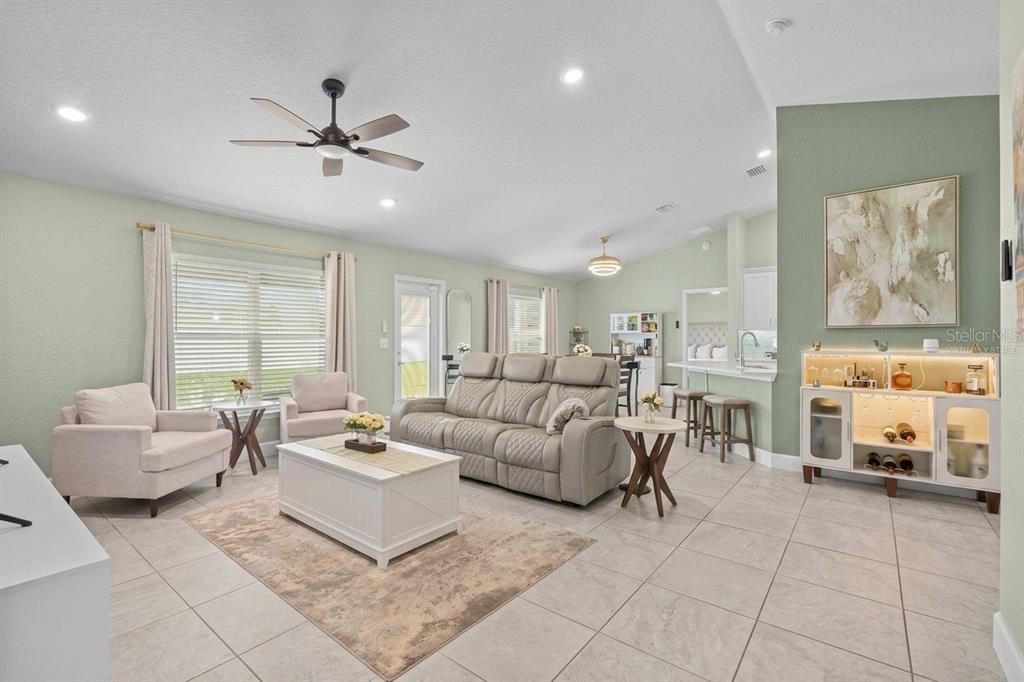 A living room with light green walls, tile flooring, a beige sofa, and a bar cabinet — 9696 SE 157TH PLACE, SUMMERFIELD, FL