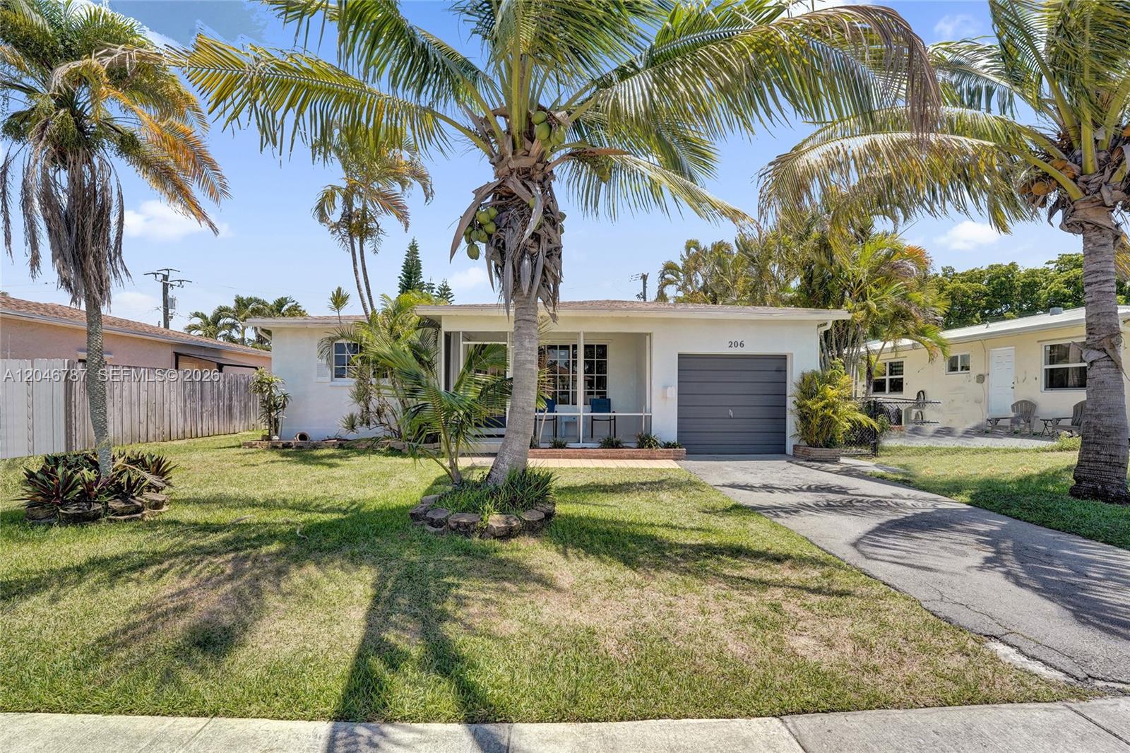 A single-story house with a gray garage door, a screened porch, and several palm trees — 206 SE 3rd St, Dania Beach FL 33004, DANIA BEACH, FL