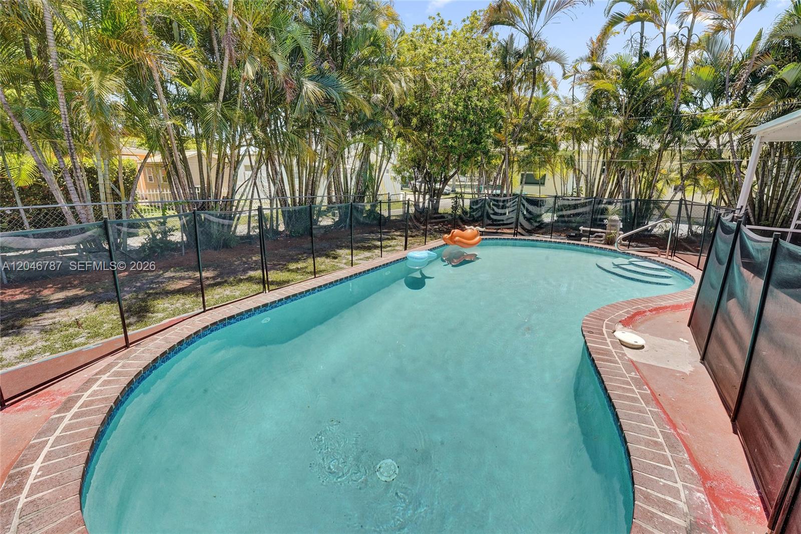 A backyard swimming pool with a brick border is enclosed by a black mesh fence — 206 SE 3rd St, Dania Beach FL 33004, DANIA BEACH, FL