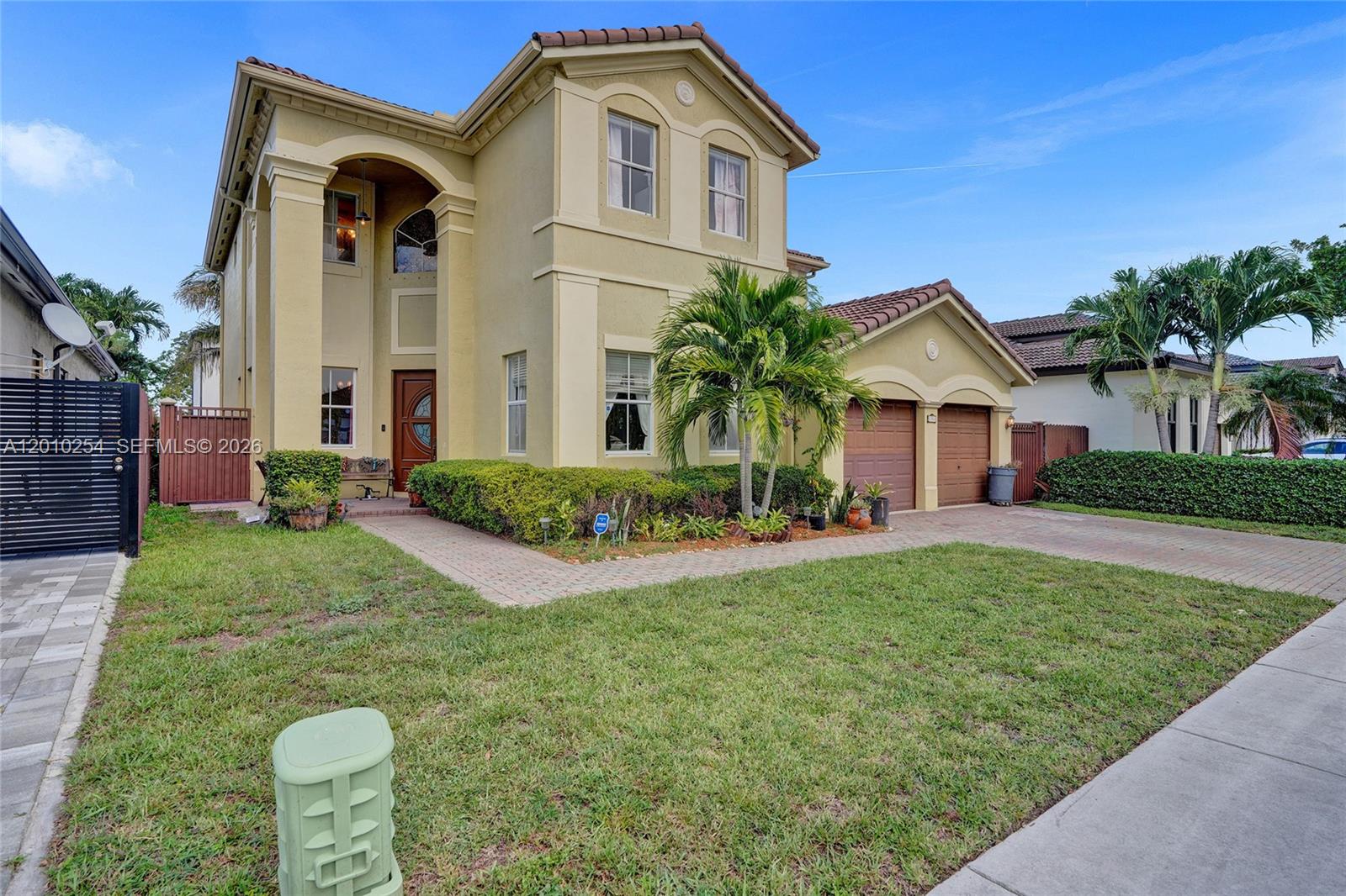 A two-story yellow stucco house features a tiled roof, arched entryway, and attached two-car garage — 17951 NW 91st Ct, Hialeah FL 33018, HIALEAH, FL