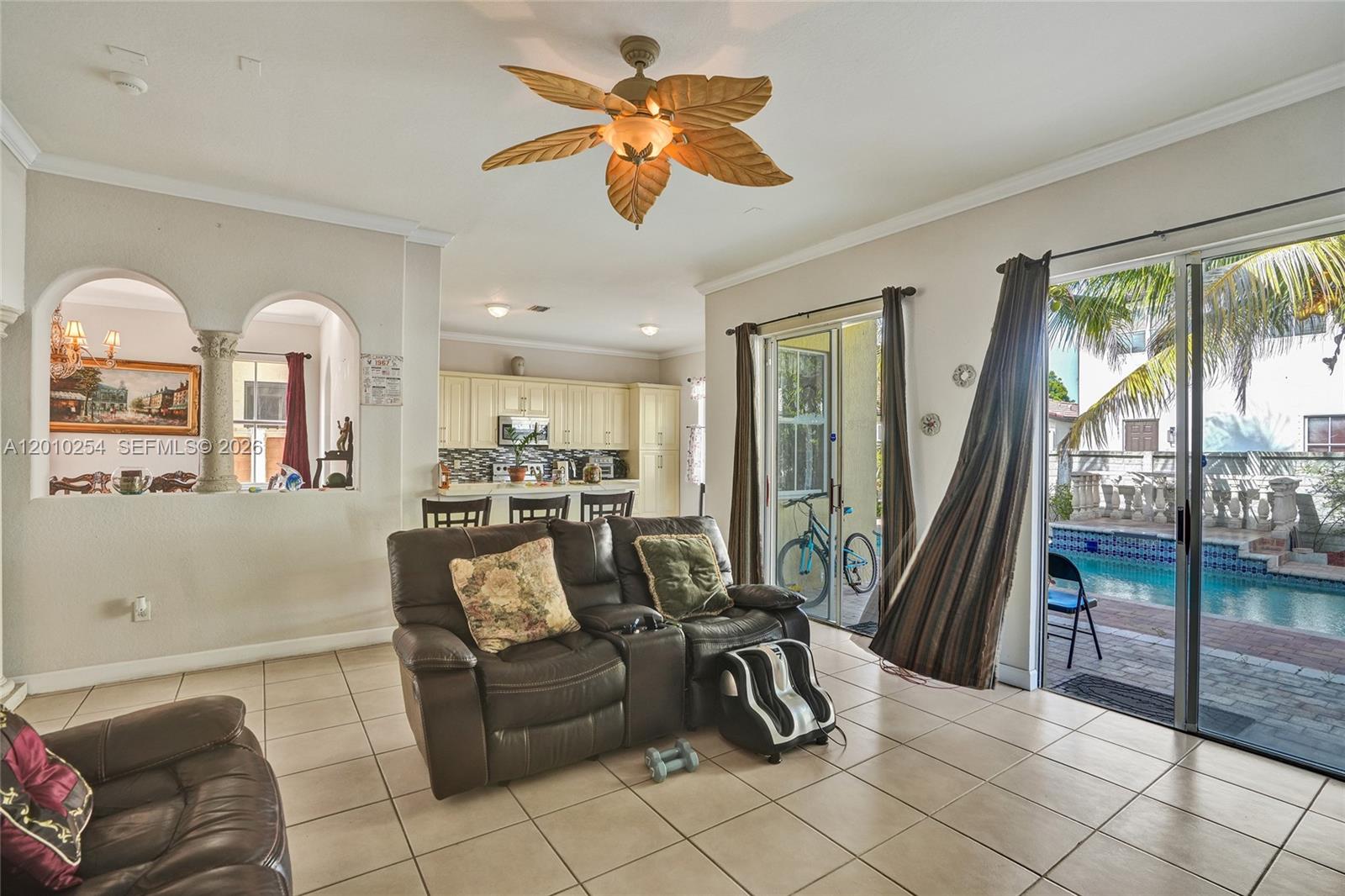 A living room with tile floors, a palm-leaf ceiling fan, and sliding doors to a pool — 17951 NW 91st Ct, Hialeah FL 33018, HIALEAH, FL