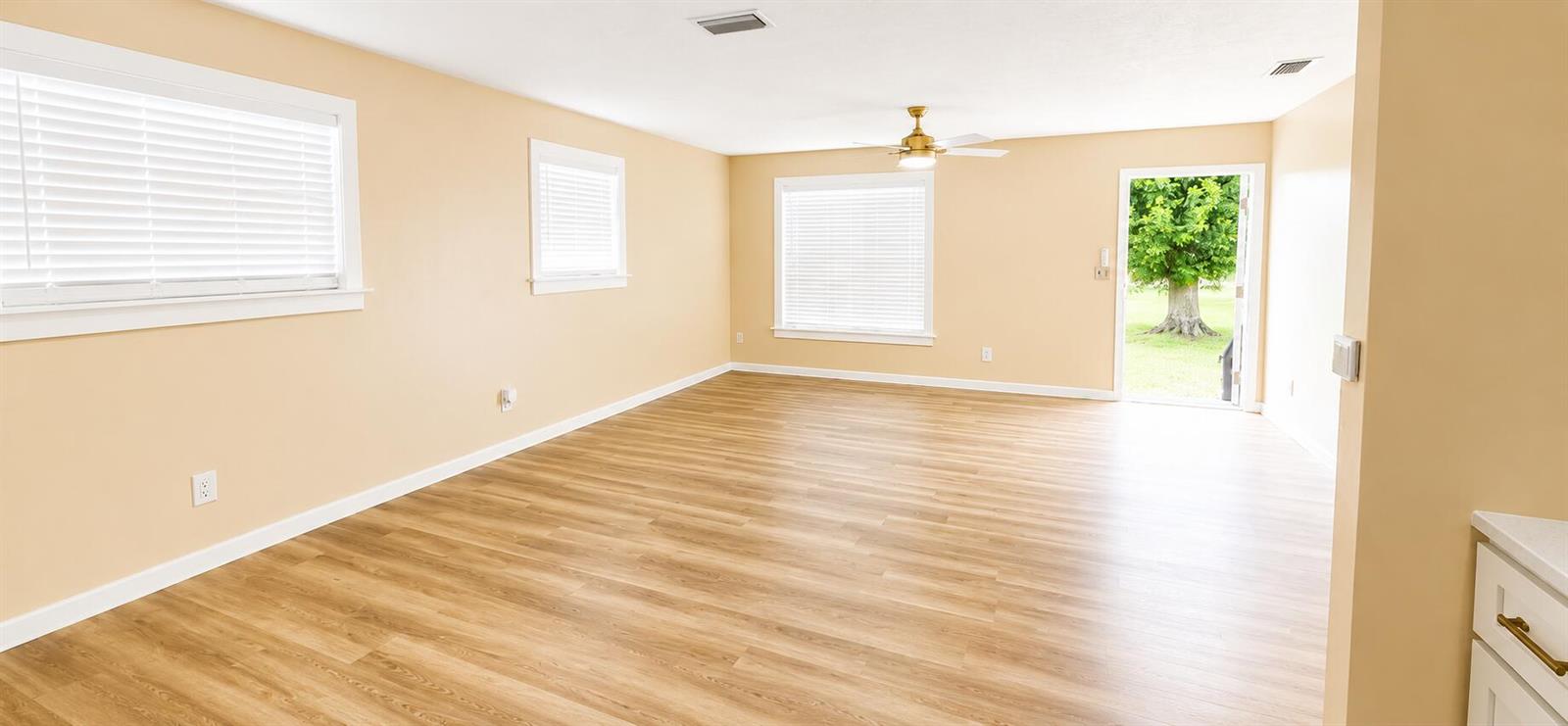 An empty living room features light-colored walls, wood-look flooring, a ceiling fan, and exterior access — 3095 NW 36th Street, Okeechobee FL 34972, OKEECHOBEE, FL