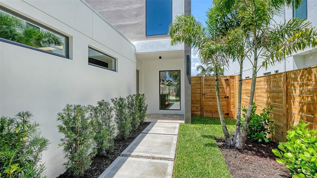 A modern white home exterior features a concrete walkway, landscaping, and a wooden privacy fence — 2225 FLORINDA STREET, SARASOTA, FL
