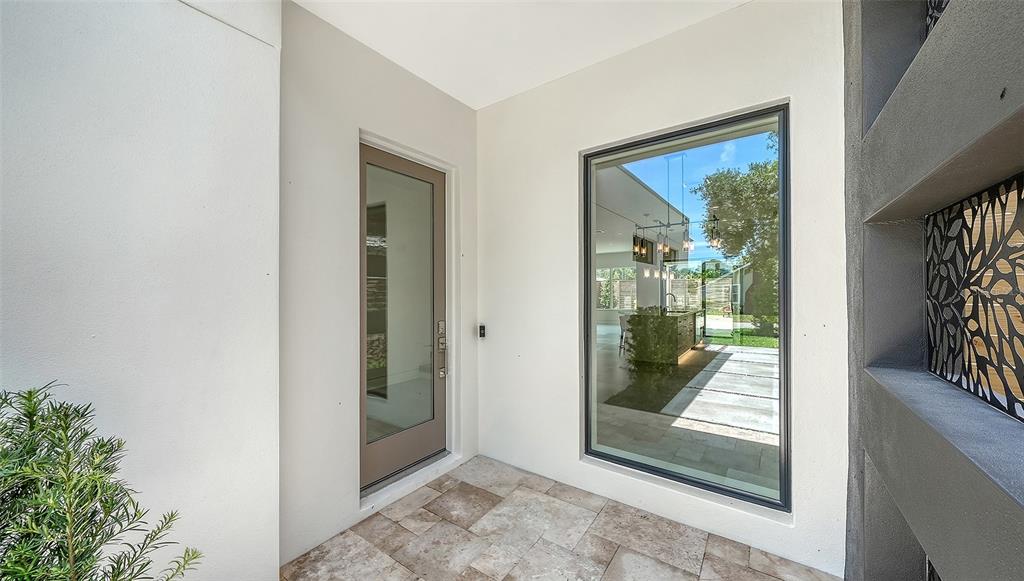 A modern entryway features a glass door, a large window, and light-colored stone flooring — 2225 FLORINDA STREET, SARASOTA, FL
