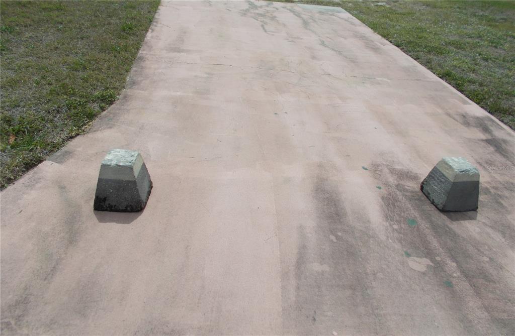 A concrete driveway features two small, weathered stone parking stops on a grassy lot — 6759 NEIGHBORLY COURT, NORTH PORT, FL
