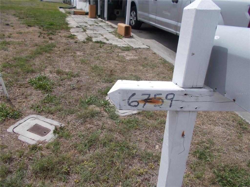A white wooden mailbox post displays the house number 6759 in a grassy front yard — 6759 NEIGHBORLY COURT, NORTH PORT, FL