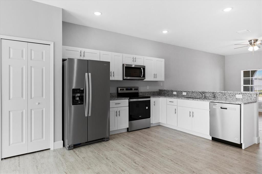 A kitchen features white cabinets, granite countertops, stainless steel appliances, and light wood-look flooring — 13 TROUT WAY UNIT A & B, KISSIMMEE, FL