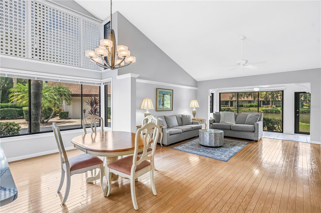 A dining area and living room with hardwood floors, vaulted ceilings, and large windows — 3174 WINDRUSH UNIT 25, SARASOTA, FL